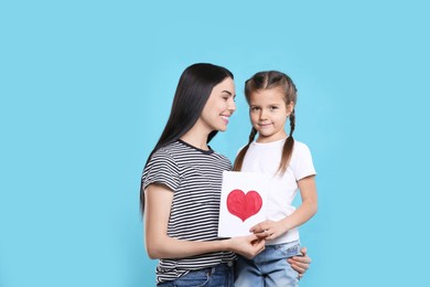 Photo of Happy woman with her cute daughter and handmade greeting card on light blue background. Mother's day celebration