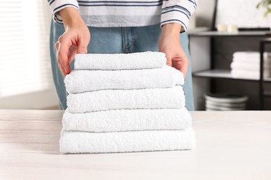 Photo of Woman stacking clean towels on white table in laundry room, closeup