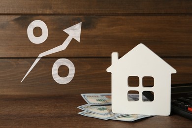 Mortgage rate rising illustrated by percent sign with upward arrow. House model, money and calculator on wooden table