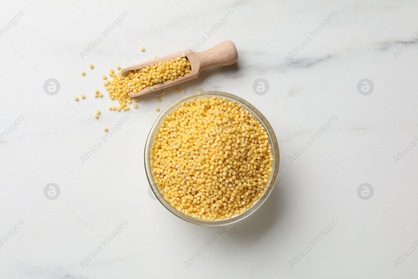 Photo of Millet groats in bowl and scoop on white marble table, flat lay