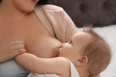 Photo of Woman breastfeeding her little baby on bed indoors