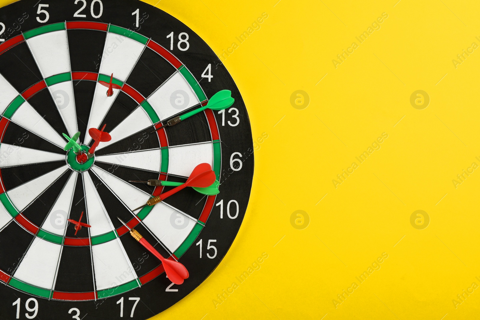 Photo of Dart board with arrows on yellow background, top view and space for text. Party game