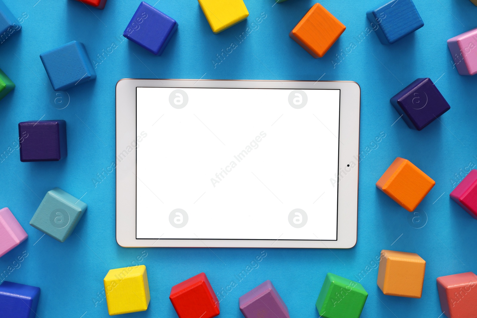 Photo of Modern tablet and cubes on light blue background, flat lay. Space for text