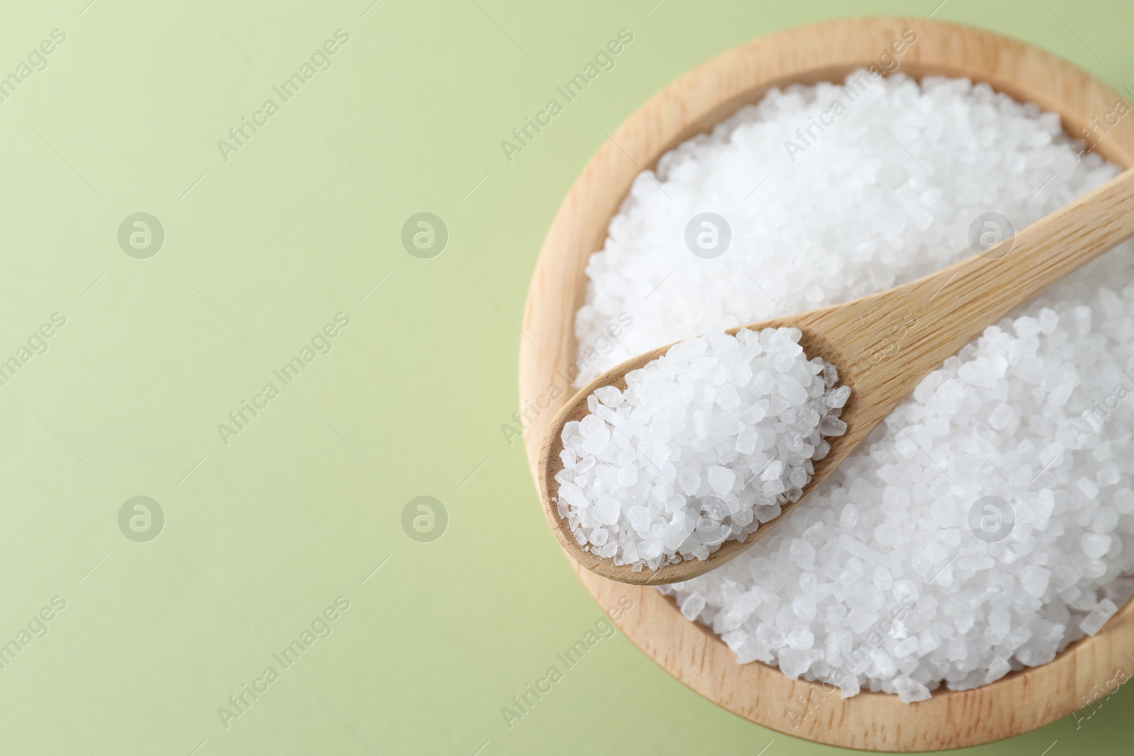 Photo of Organic white salt in bowl and spoon on olive background, top view. Space for text