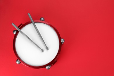 Drum and sticks on red background, top view with space for text. Percussion musical instrument