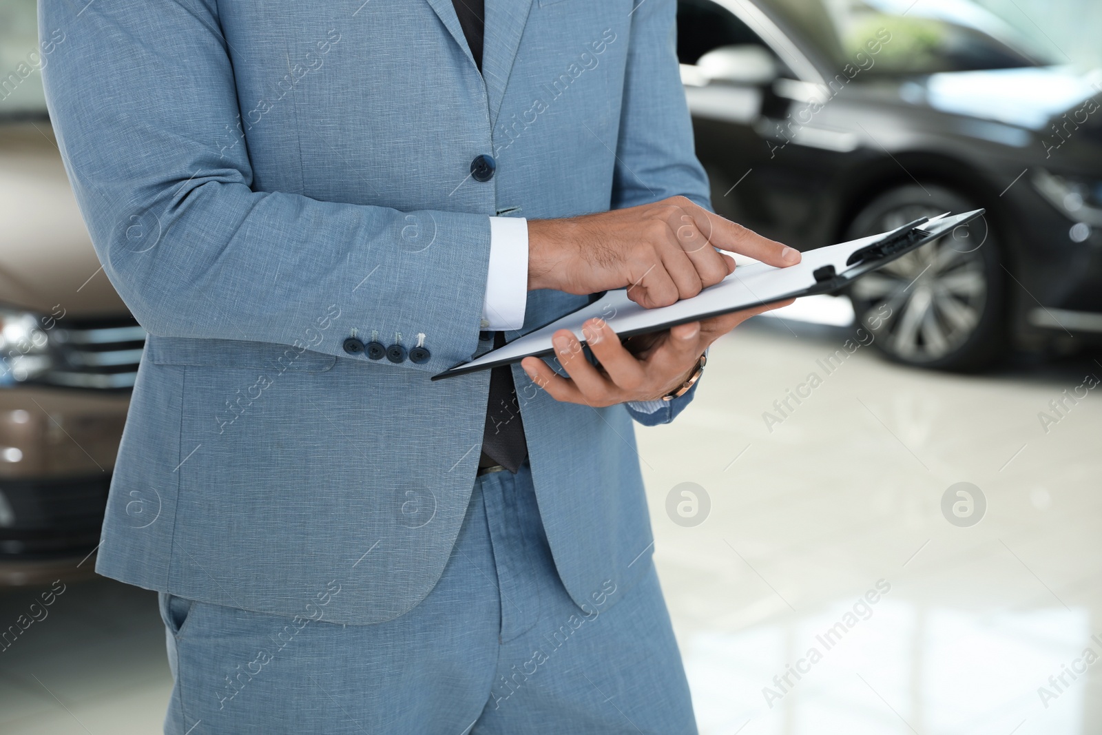 Photo of Young salesman with clipboard in modern car dealership, closeup
