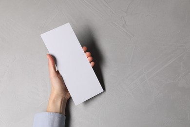 Photo of Woman holding blank card at light grey table, top view. Mockup for design