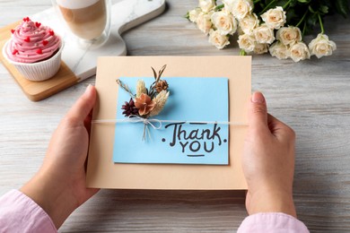 Woman holding card with phrase Thank you at wooden table, closeup
