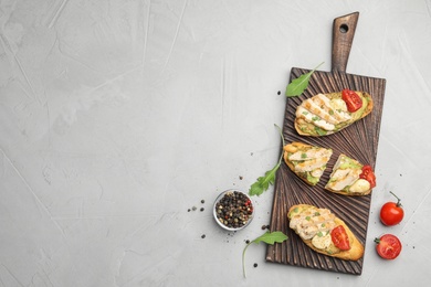 Photo of Board with delicious chicken bruschettas on light grey table, flat lay. Space for text