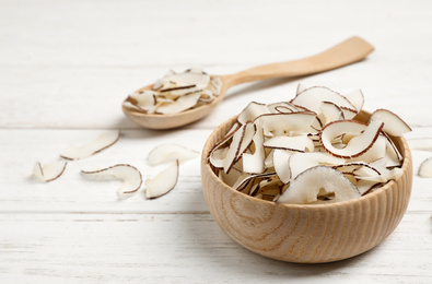 Tasty coconut chips on white wooden table. Space for text