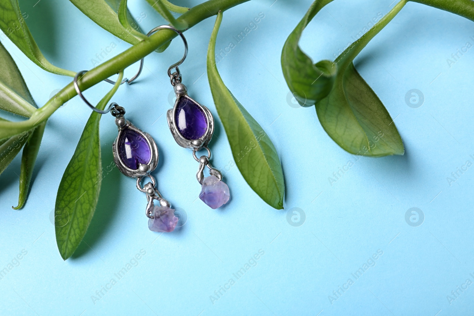 Photo of Beautiful pair of silver earrings with amethyst gemstones and leaves on light blue background, above view