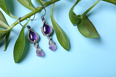 Photo of Beautiful pair of silver earrings with amethyst gemstones and leaves on light blue background, above view