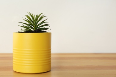 Photo of Echeveria plant in yellow tin can on wooden table, closeup. Space for text