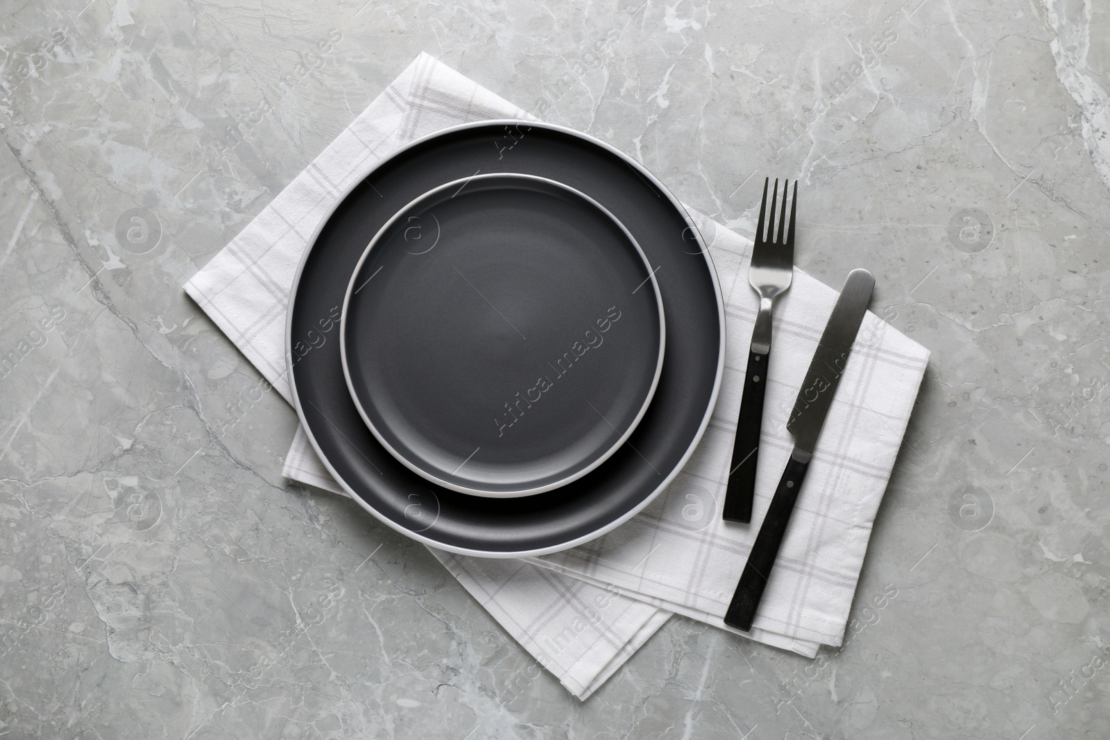 Photo of New dark plates with cutlery and napkin on light grey marble table, flat lay