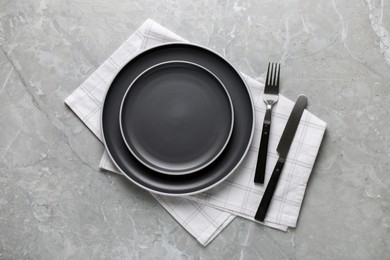 Photo of New dark plates with cutlery and napkin on light grey marble table, flat lay