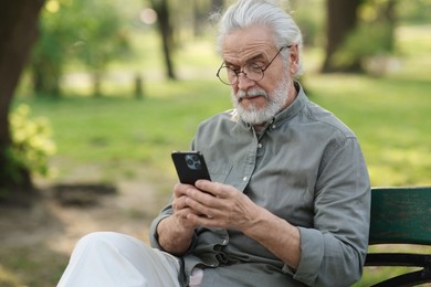 Photo of Portrait of happy grandpa with glasses using smartphone on bench in park