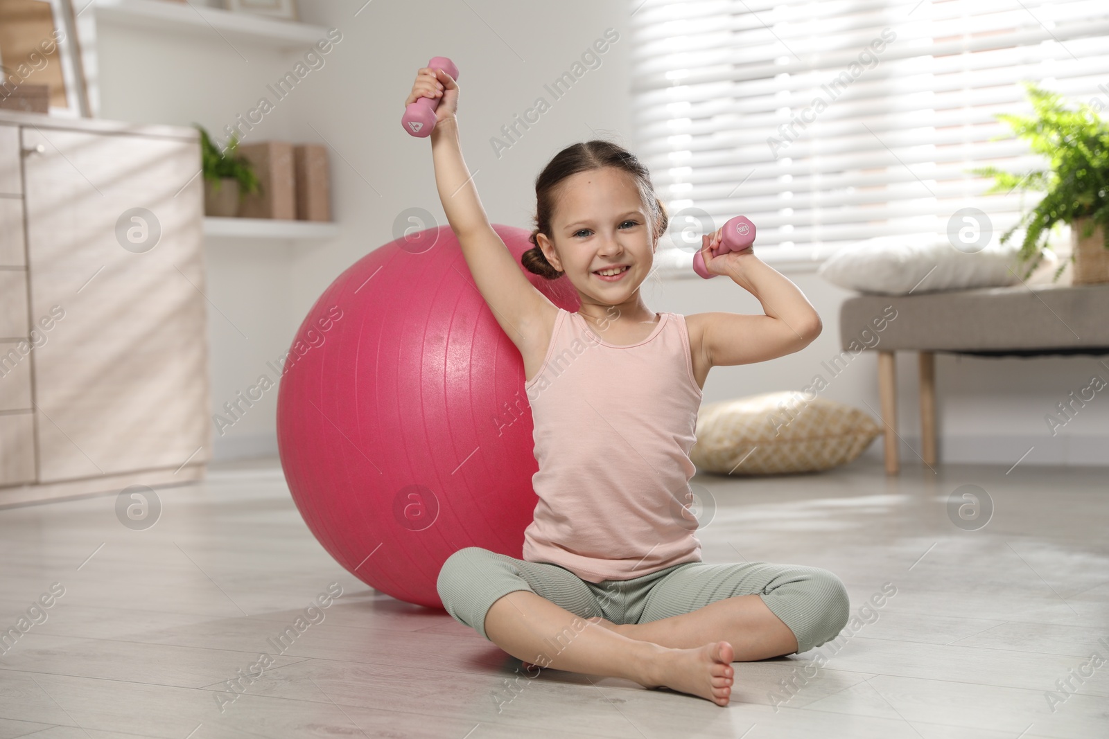 Photo of Cute little girl with dumbbells near fit ball at home