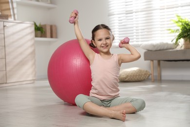 Photo of Cute little girl with dumbbells near fit ball at home