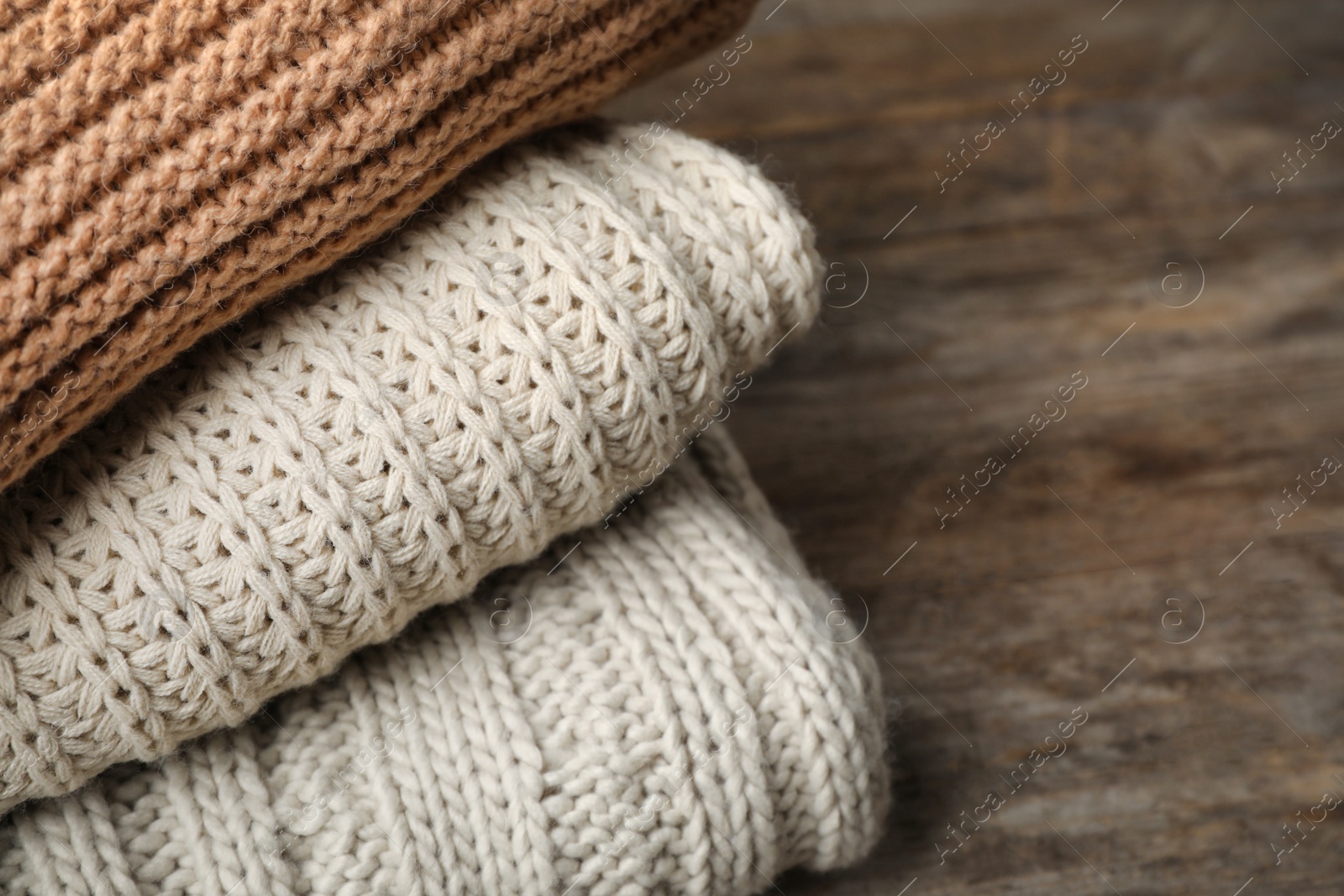 Photo of Stack of folded knitted sweaters on table, closeup. Space for text