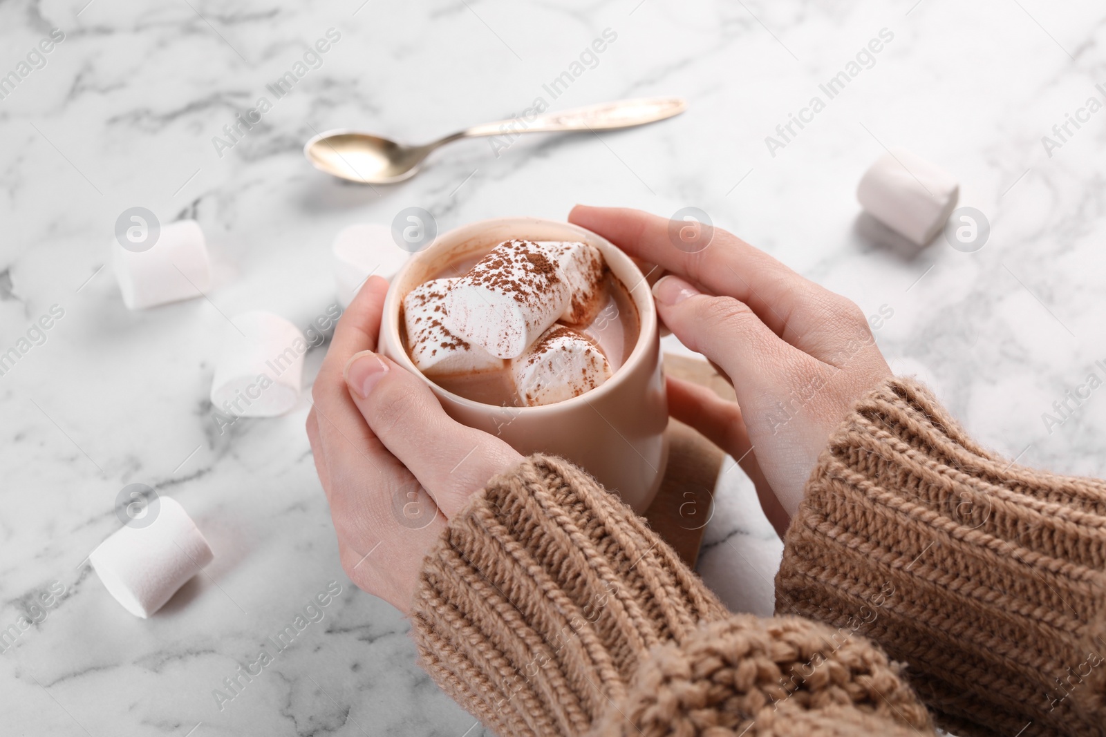 Photo of Woman drinking aromatic hot chocolate with marshmallows and cocoa powder at white marble table, closeup