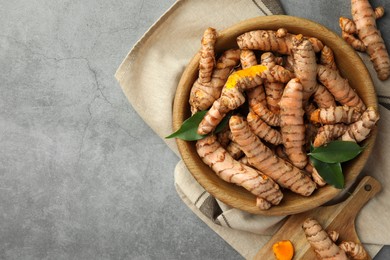 Photo of Many raw turmeric roots and green leaves on grey table, flat lay. Space for text