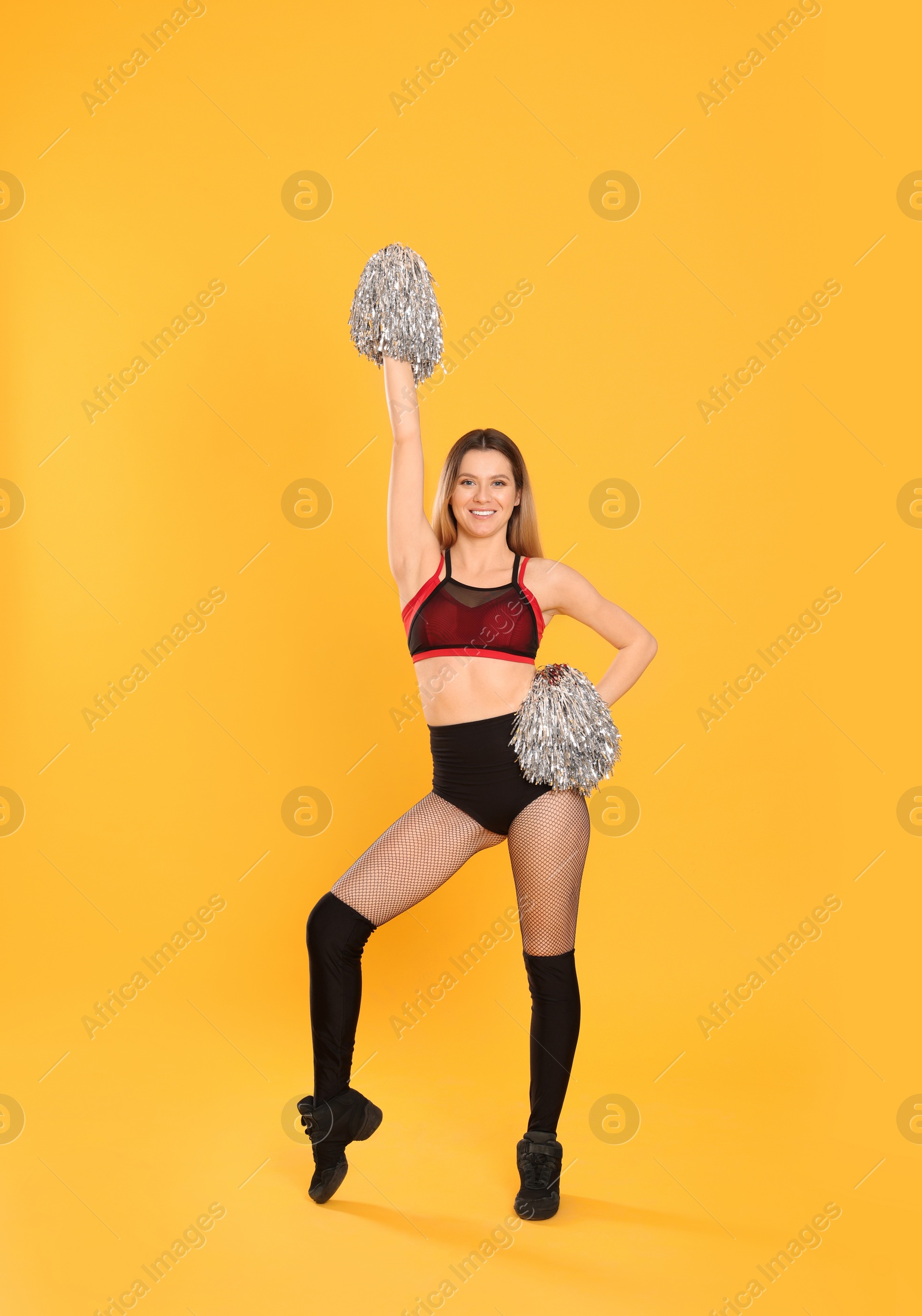 Photo of Beautiful cheerleader in costume holding pom poms on yellow background