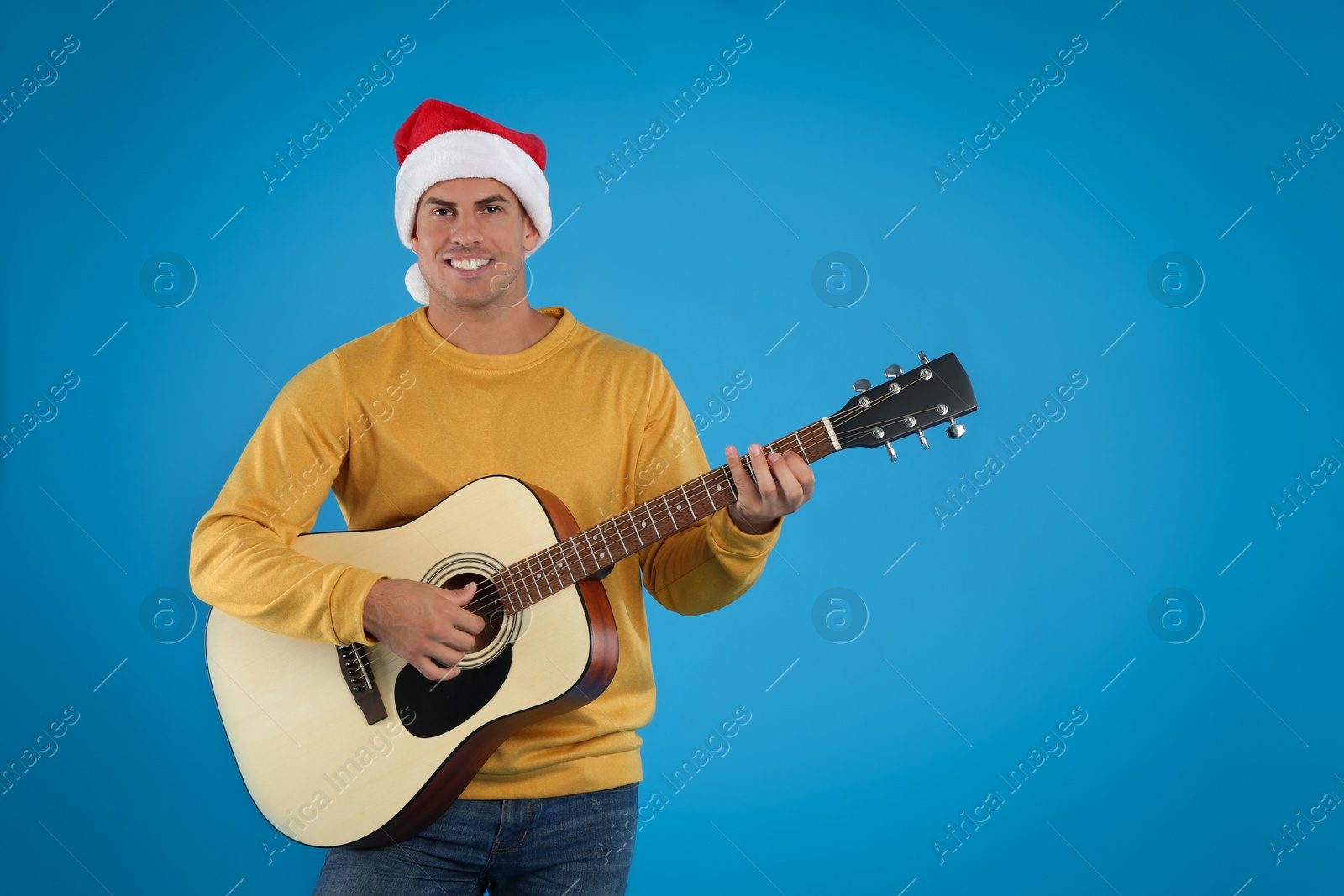 Photo of Man in Santa hat playing acoustic guitar on light blue background. Christmas music