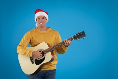 Photo of Man in Santa hat playing acoustic guitar on light blue background. Christmas music
