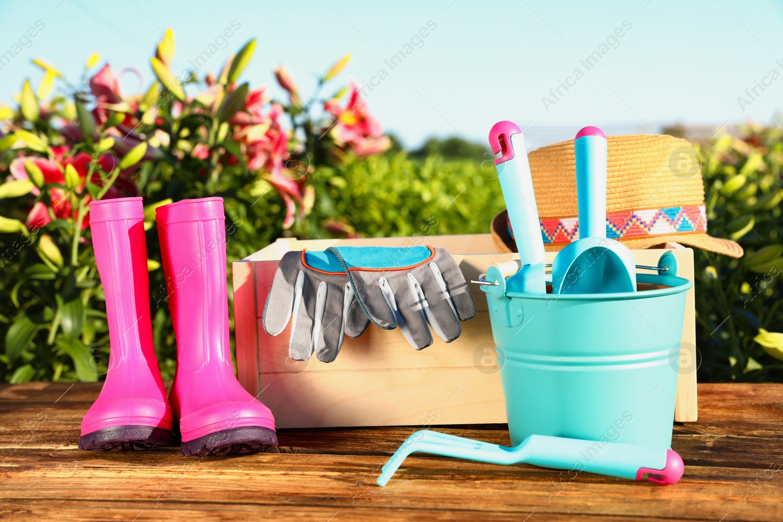Photo of Rubber boots and gardening tools on wooden table at lily field