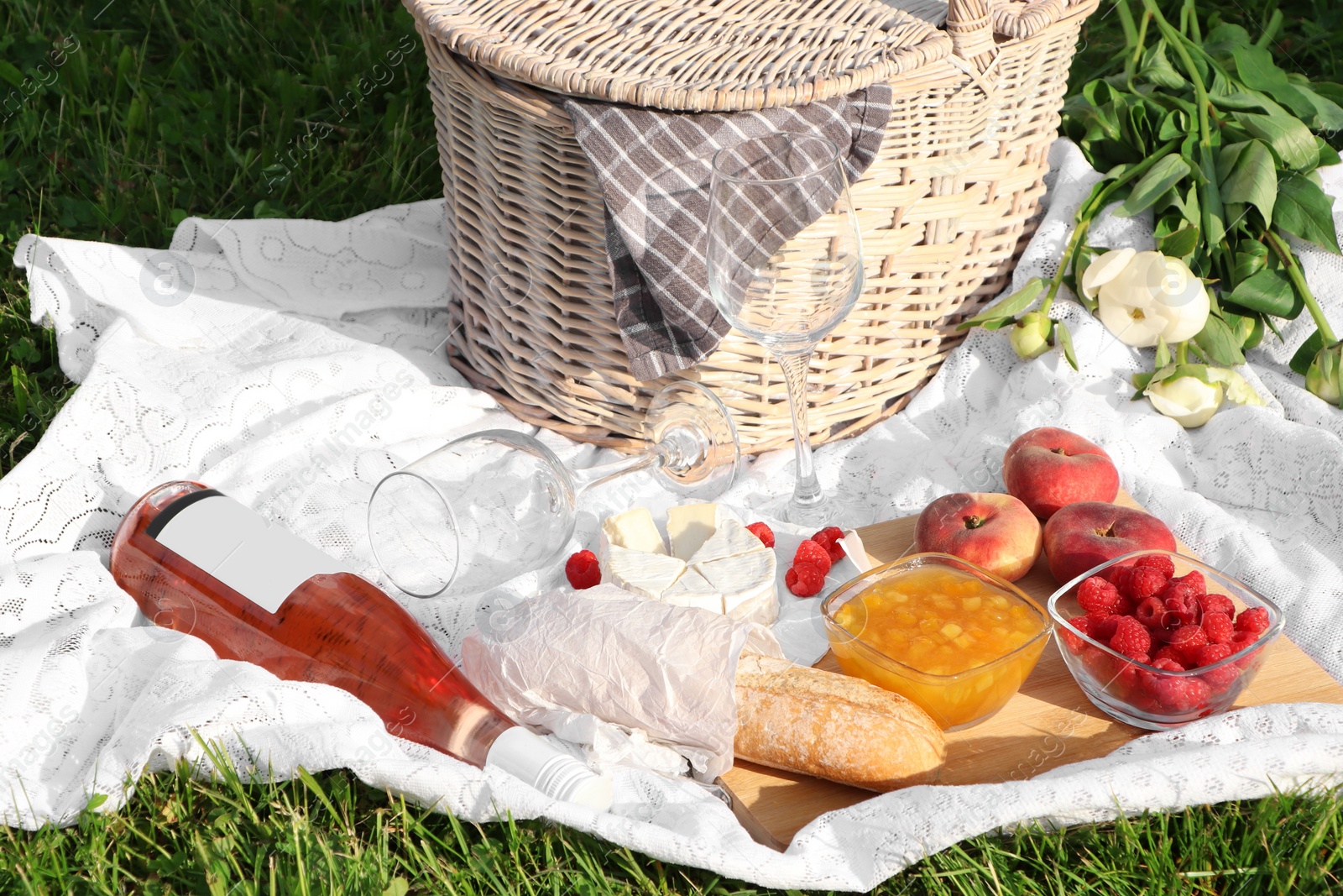 Photo of Picnic blanket with tasty food, flowers, basket and cider on green grass outdoors