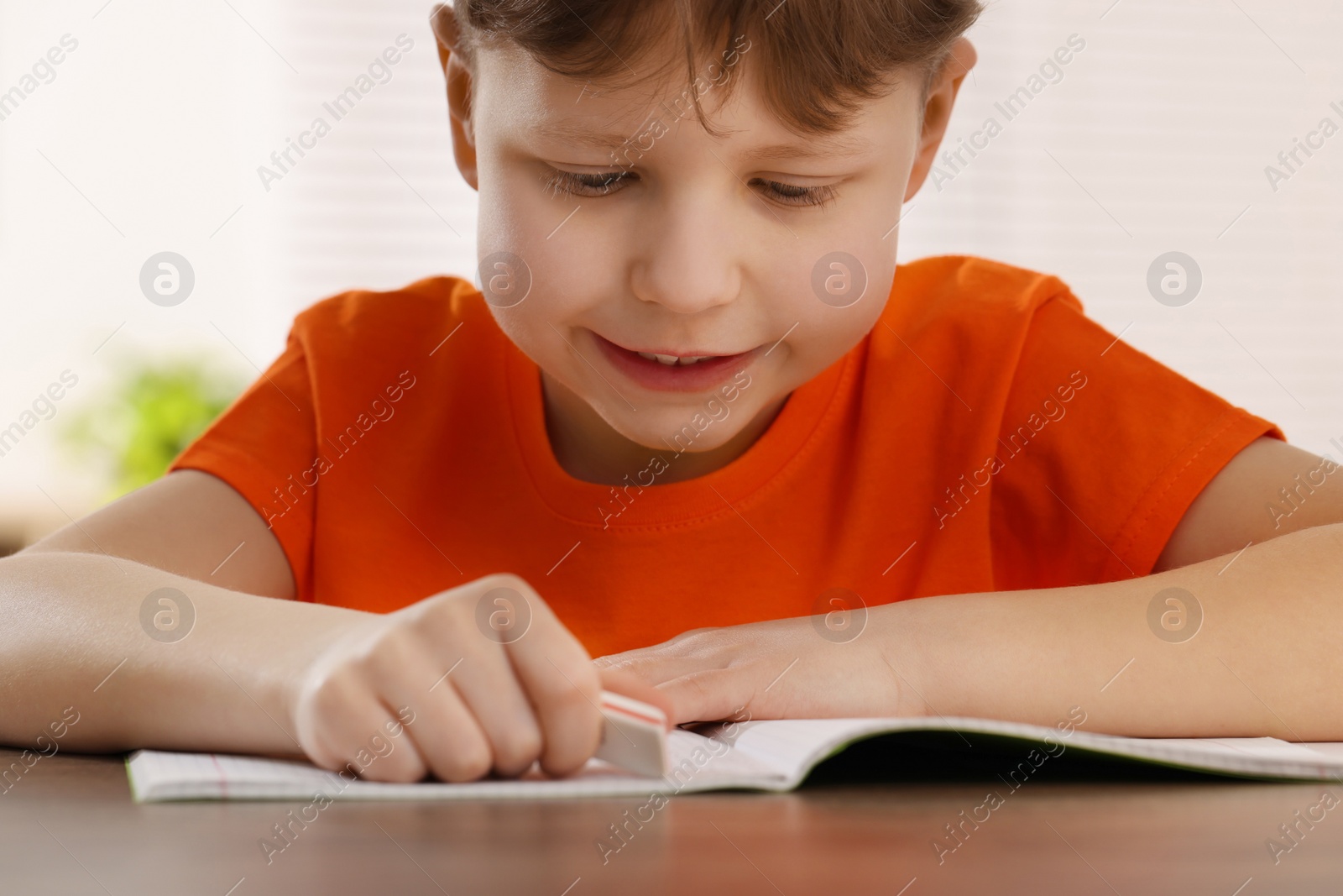 Photo of Little boy erasing mistake in his notebook at wooden desk