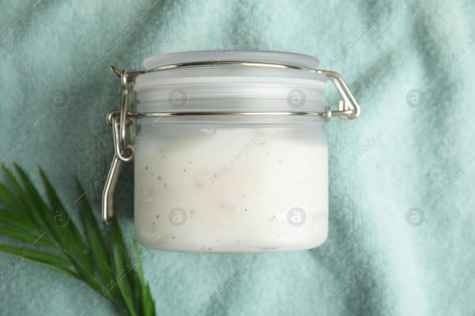 Photo of Jar of salt scrub and palm leaf on green towel, flat lay