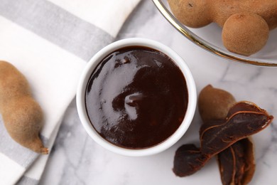 Photo of Bowl of tamarind sauce and fresh pods on white marble table, flat lay