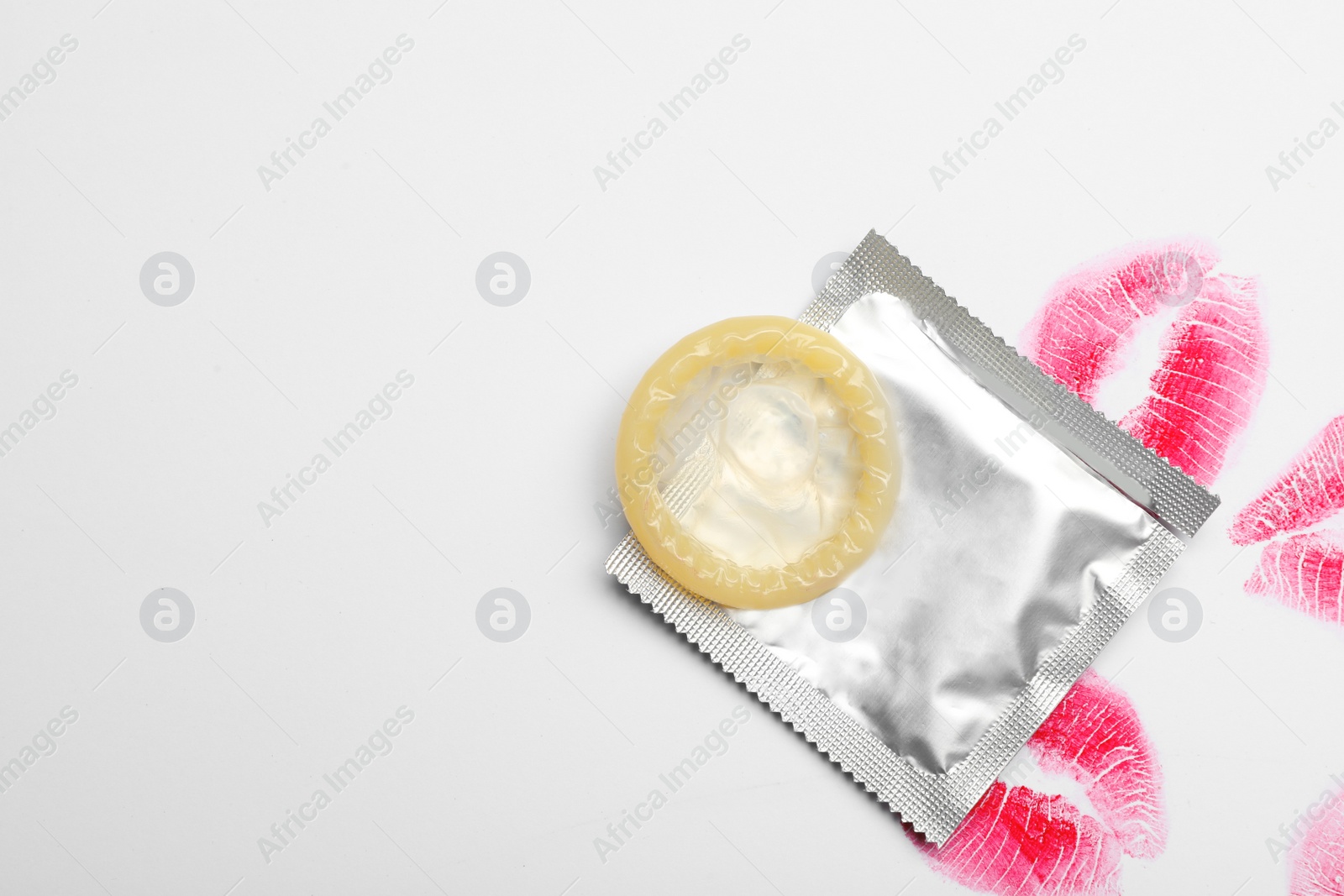 Photo of Condom and lipstick kiss marks on white background, top view. Safe sex