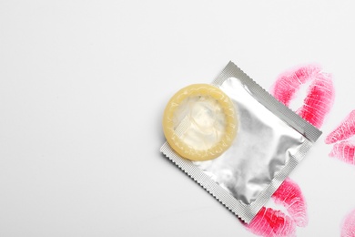 Condom and lipstick kiss marks on white background, top view. Safe sex