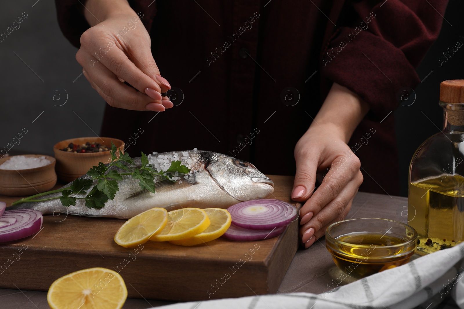 Photo of Woman adding spices onto raw dorado fish at grey table, closeup