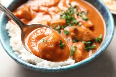 Spoon with tasty butter chicken over bowl of meal, closeup