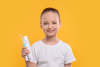 Photo of Happy girl holding electric toothbrush and tube of toothpaste on yellow background