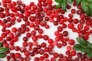Photo of Frozen red cranberries and green leaves on white background, flat lay