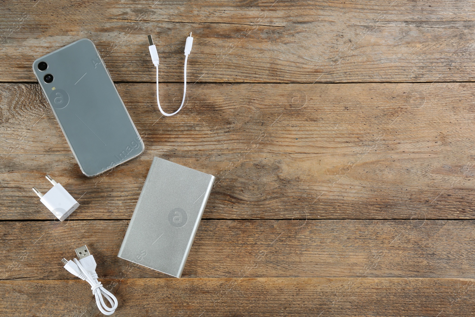 Photo of Flat lay composition with mobile phone and portable charger on wooden background. Space for text