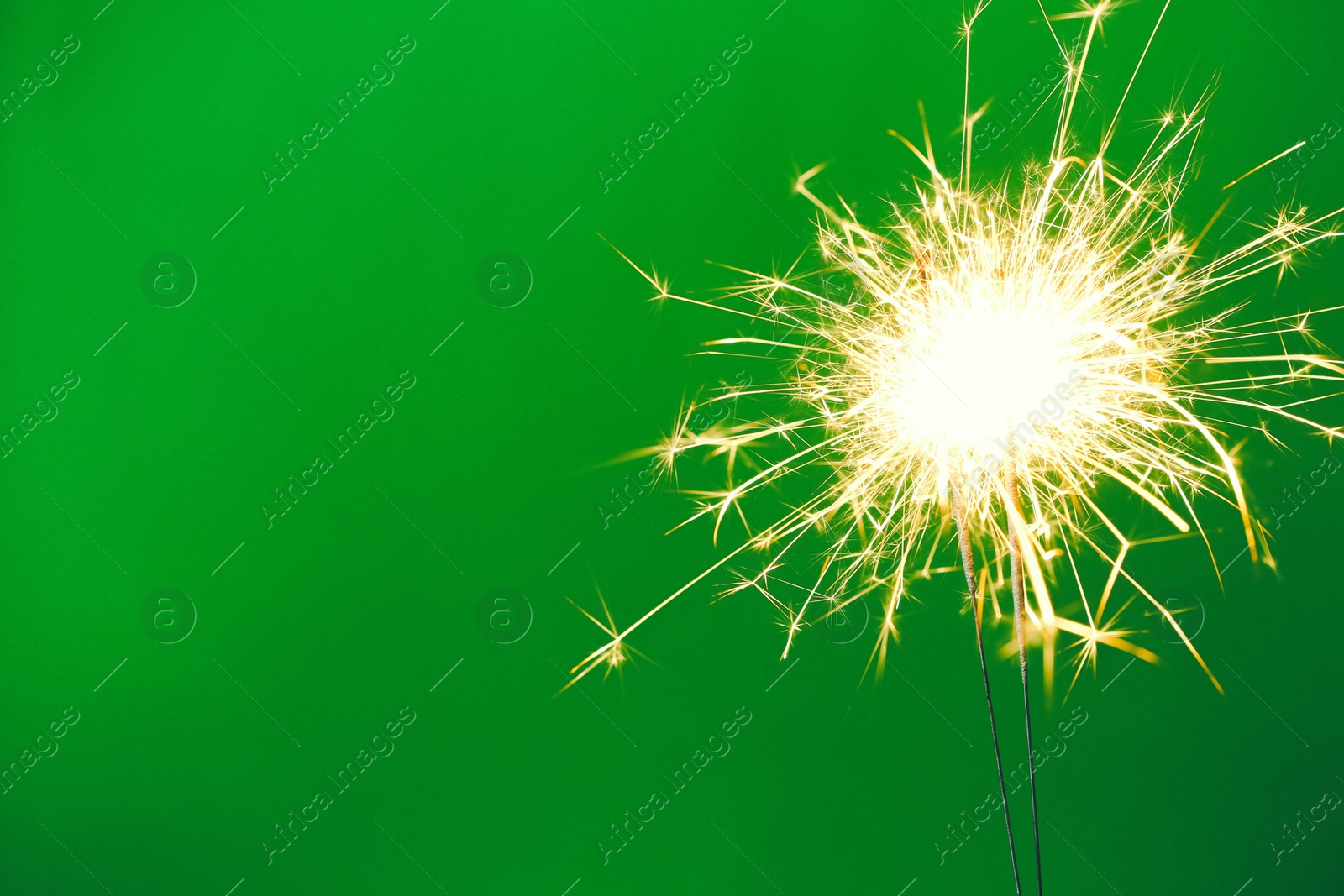 Photo of Bright burning sparklers on green background, closeup. Space for text