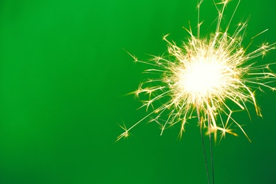 Photo of Bright burning sparklers on green background, closeup. Space for text