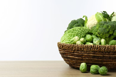 Photo of Wicker bowl with different types of fresh cabbage on wooden table against white background. Space for text