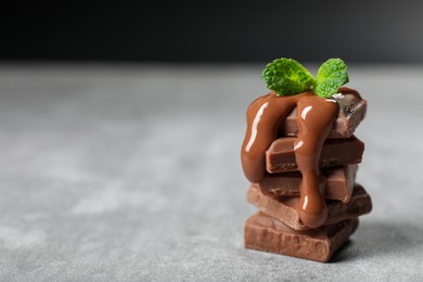 Photo of Pieces of milk chocolate with tasty paste and mint on gray table, closeup. Space for text
