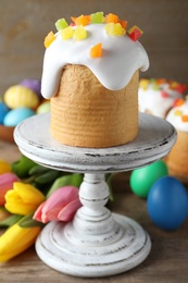 Stand with traditional Easter cake, tulips and colorful eggs on wooden table