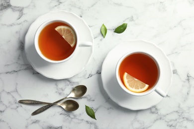 Photo of Cups with black tea and lemon on marble table, top view