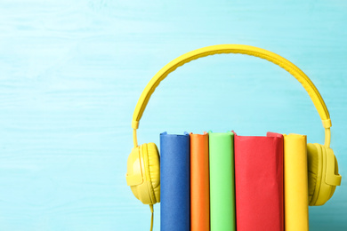 Books and modern headphones on light blue wooden background, closeup. Space for text