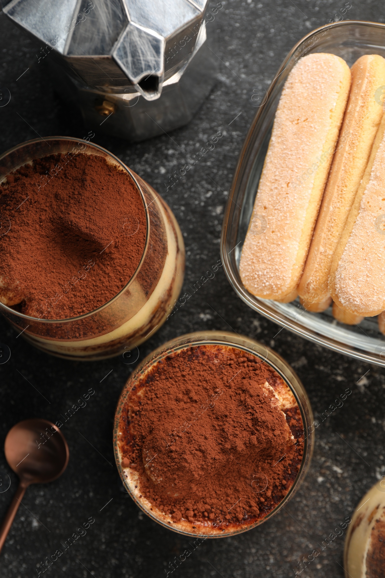 Photo of Delicious tiramisu in glasses and ingredients on grey textured table, flat lay