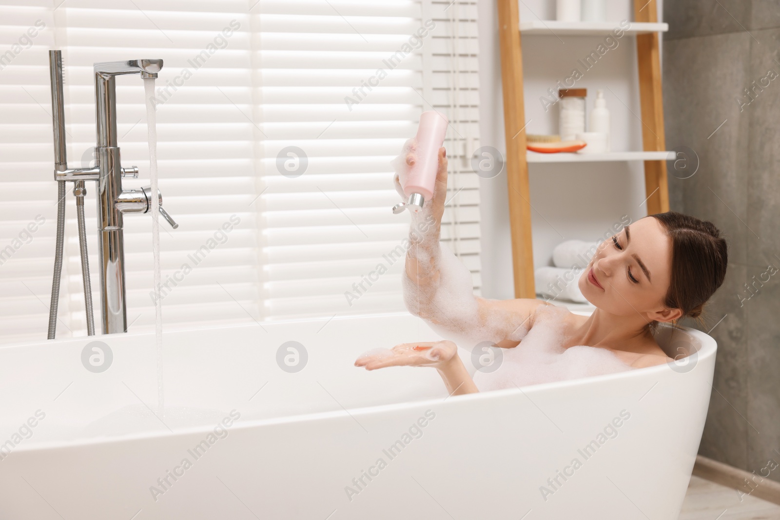 Photo of Woman pouring shower gel onto hand in bath indoors