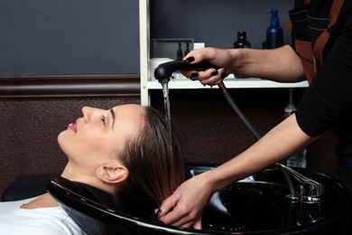 Photo of Professional hairdresser washing woman's hair at sink in salon